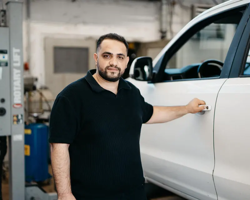 Müslüm Kurnaz neben einem weißen Fahrzeug in der Werkstatt